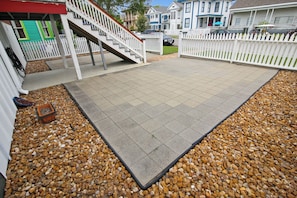 A patio area with a tiled floor, surrounded by a white picket fence, and a small staircase leading to a green door.