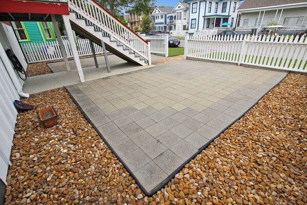 Um espaço de pátio com piso de azulejos, cercado por uma cerca branca de piquete, e uma pequena escadaria que leva a uma porta verde.