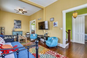 A living room with a sofa, chairs, a coffee table, and a TV. There is a staircase leading to another room.