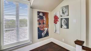 A hallway with a large window, a painting of a woman in a red dress, and two smaller portraits on the wall. - Abfab Seaside Cottage by Ryson Vacation Rentals (Galveston)