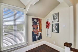 A hallway with a large window, a painting of a woman in a red dress, and two smaller portraits on the wall. - Abfab Seaside Cottage by Ryson Vacation Rentals (Galveston)