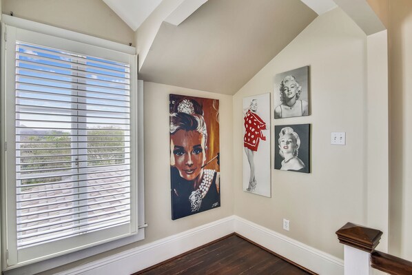 A hallway with a large window, a painting of a woman in a red dress, and two smaller portraits on the wall. - Abfab Seaside Cottage by Ryson Vacation Rentals (Galveston)