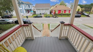 A porch with a yellow chair, a white picket fence, and a view of houses in the background. - Abfab Seaside Cottage by Ryson Vacation Rentals (Galveston)