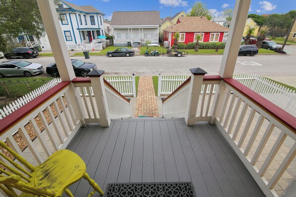 A porch with a yellow chair, a white picket fence, and a view of houses in the background.