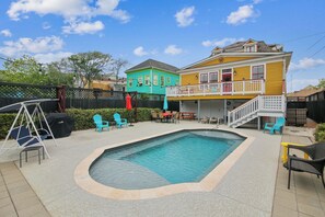 A backyard with a swimming pool, outdoor furniture, and a two-story house with a balcony. - Abfab Seaside Cottage by Ryson Vacation Rentals (Galveston)