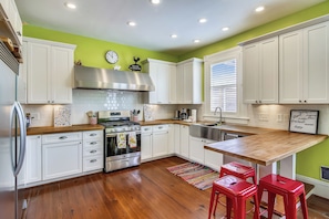 A modern kitchen with white cabinets, a stainless steel range hood, a wooden countertop, and a red rug. - Abfab Seaside Cottage by Ryson Vacation Rentals (Galveston)