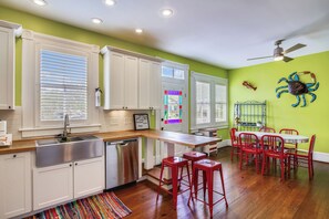 A kitchen with white cabinets, a stainless steel sink, and a wooden countertop. There is a red bar stool and a dining table with red chairs.