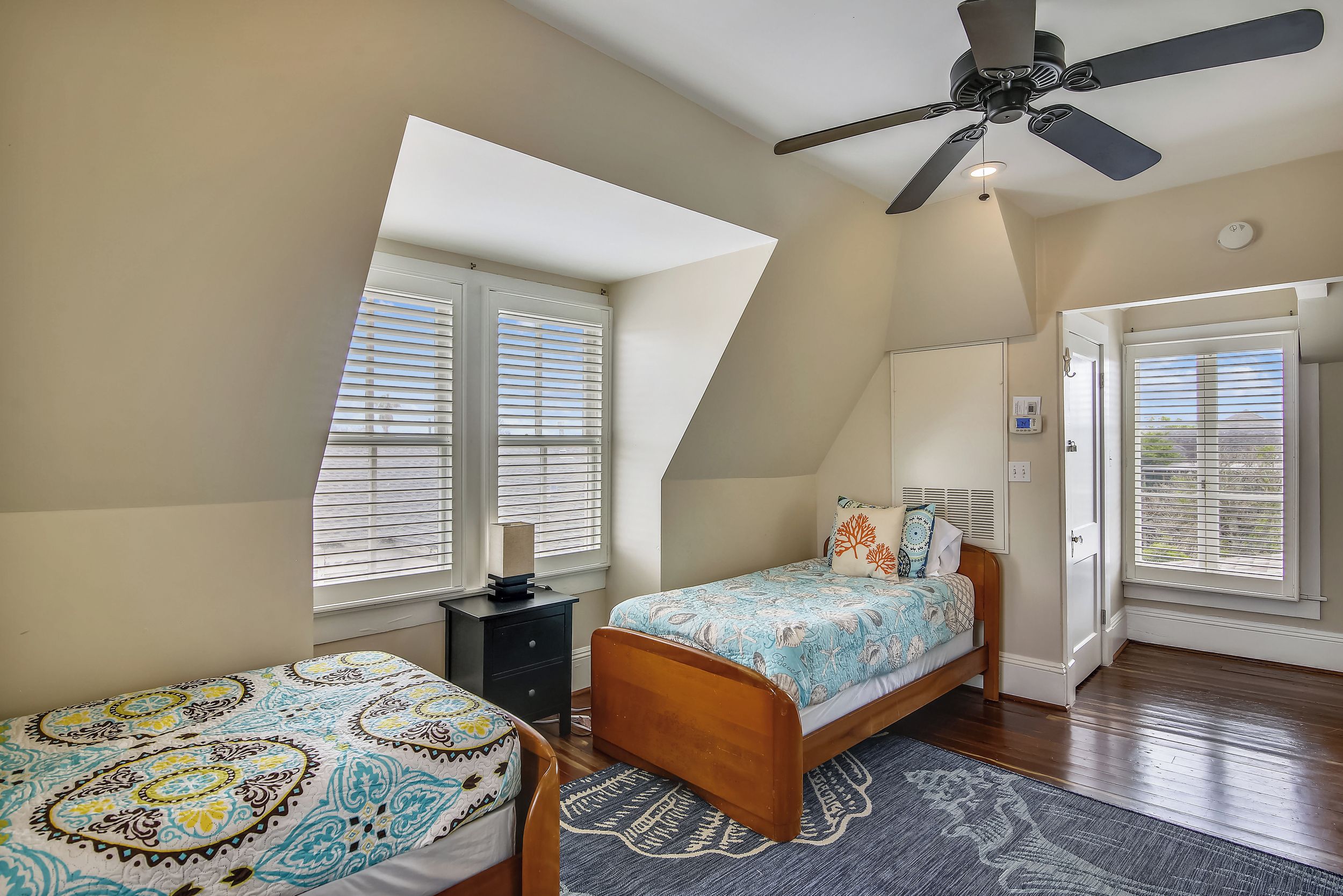 A bedroom with two beds, a ceiling fan, and large windows.