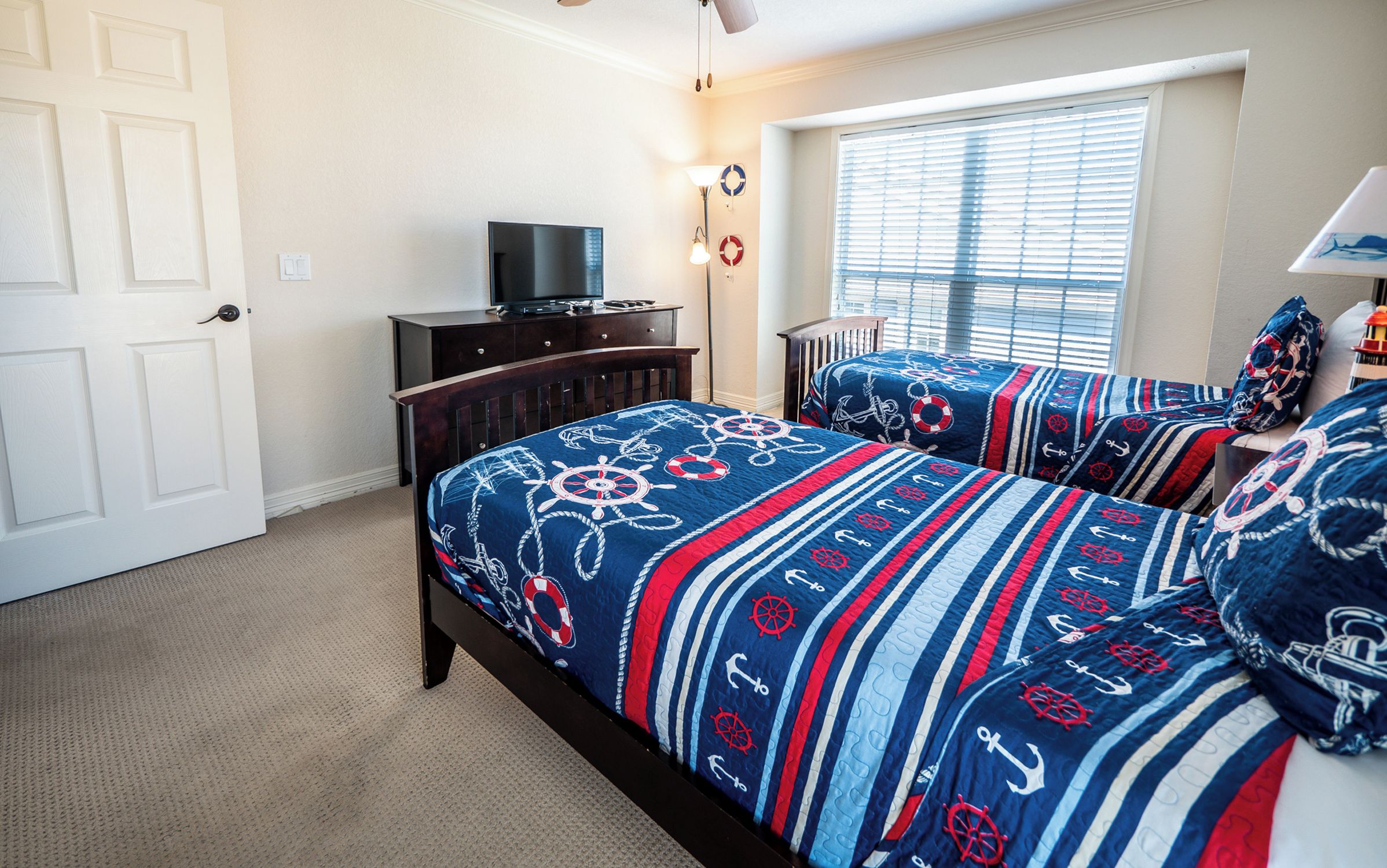 A bedroom with two beds, a dresser, a TV, and a window with blinds.