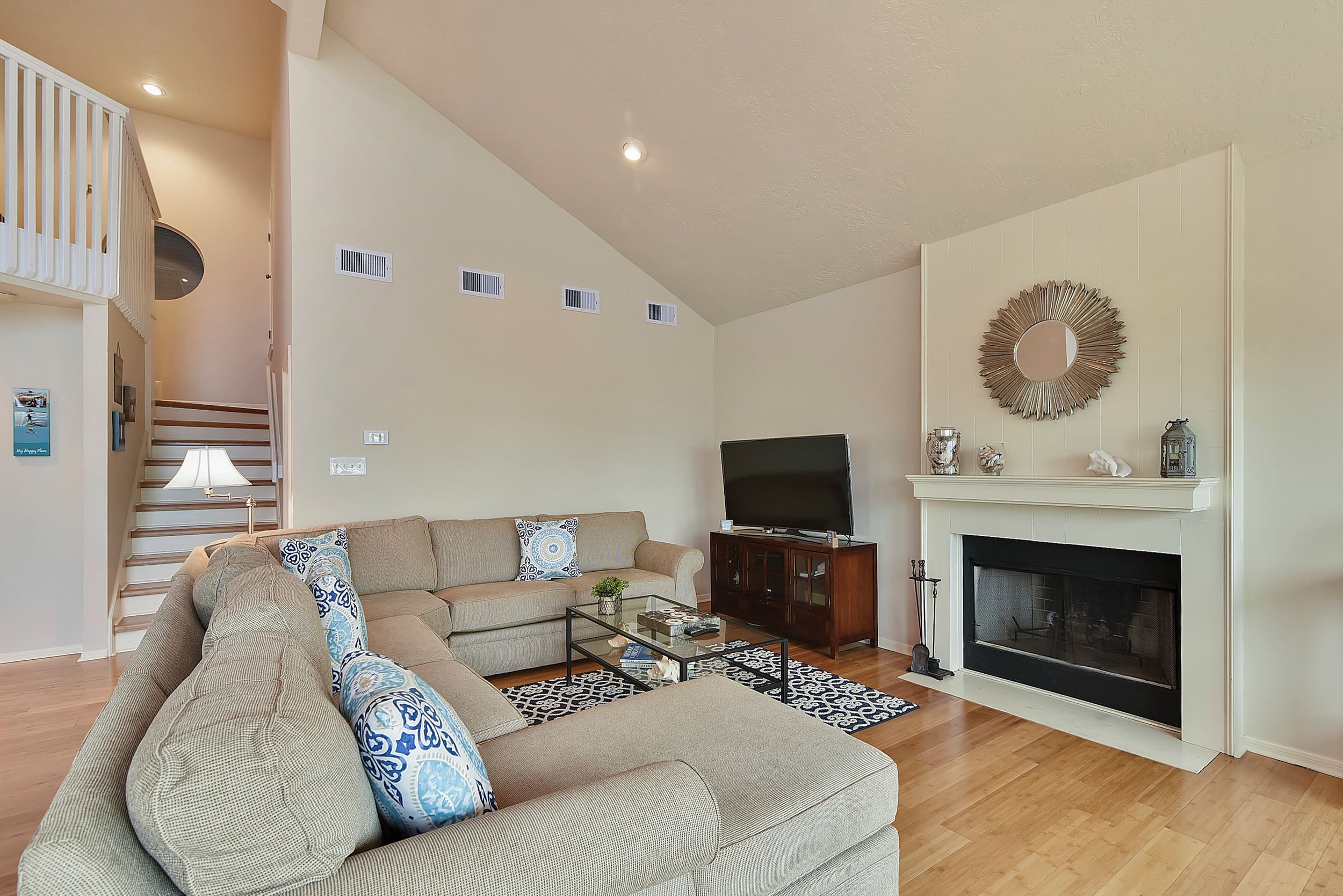 A living room with a sectional sofa, a flat-screen TV, a fireplace, and a staircase leading to an upper level.