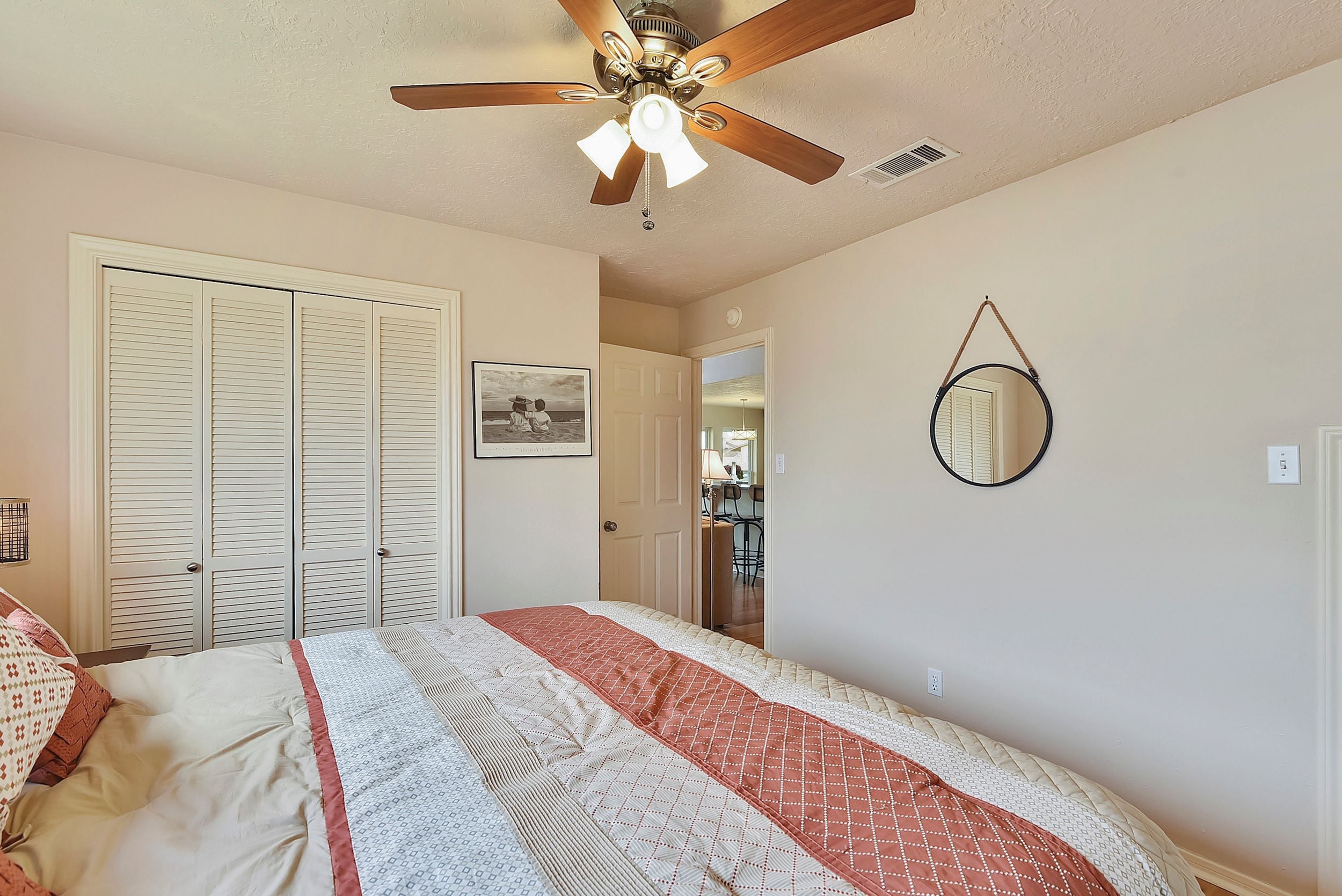 A bedroom with a bed, a ceiling fan, a door, and a mirror on the wall.