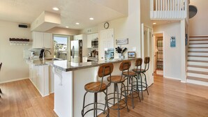 A modern kitchen with white cabinetry, a granite countertop, and a bar area with stools. - All Decked Out by Ryson Vacation Rentals (Galveston)
