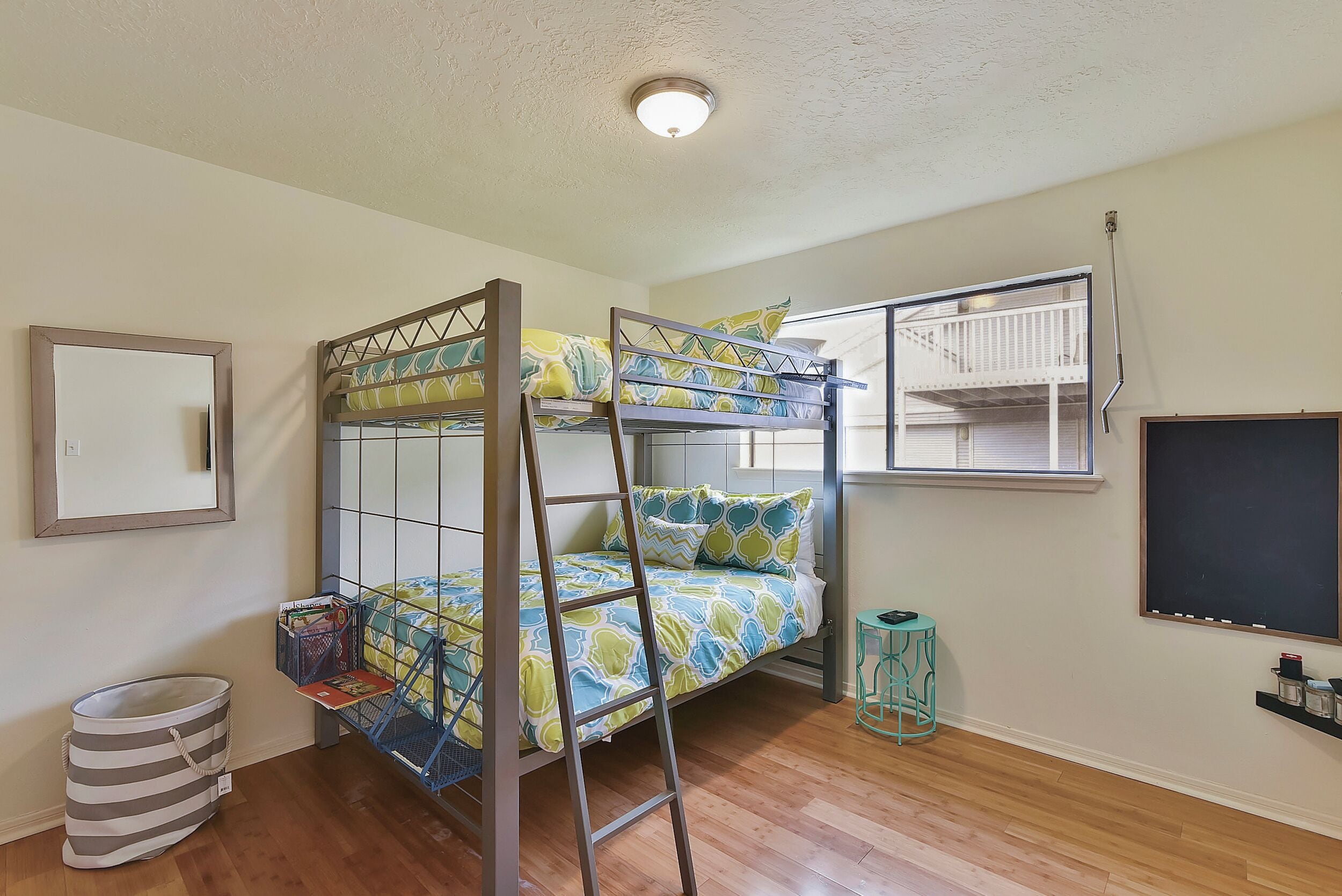A bunk bed room with a window, a small table, and a trash bin.