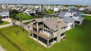 A residential area with a two-story house featuring a balcony, a driveway, and a well-maintained lawn. - All Decked Out by Ryson Vacation Rentals (Galveston)