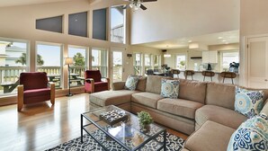A spacious living room with a large sectional sofa, a glass coffee table, and a ceiling fan. - All Decked Out by Ryson Vacation Rentals (Galveston)