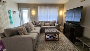 A living room with a sectional sofa, ottoman, TV stand, and a patterned rug. - Sarasota-Indian Beach Zen Home (private-pet friendly)  (Sarasota)