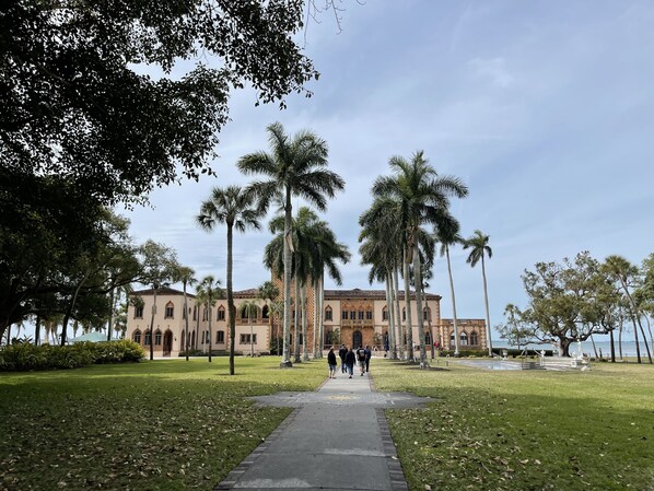 A pathway leading to a building with a symmetrical facade, palm trees, and a clear sky.