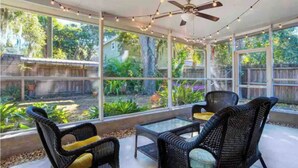 A covered patio with wicker furniture and string lights, overlooking a garden and a wooden fence. - Sarasota-Indian Beach Zen Home (private-pet friendly)  (Sarasota)