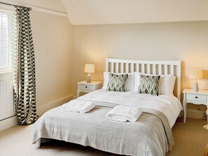 A neatly made bed with a patterned bedspread, two bedside lamps, and a window with curtains.