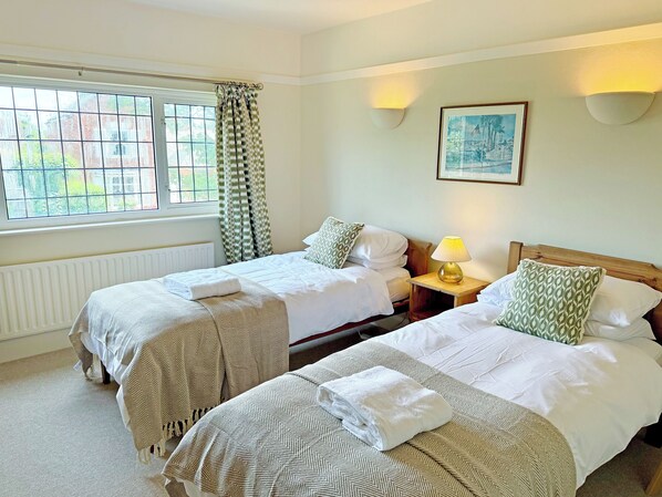 A hotel room with two beds, a window with curtains, a wall-mounted lamp, and a framed picture.