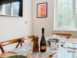Une table à manger dressée avec des verres en cristal, une bouteille de Prosecco et une affiche encadrée accrochée au mur.