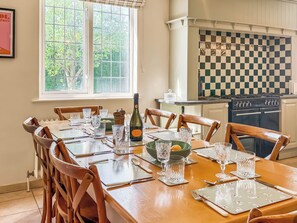 A dining table set for six with chairs, a bottle of champagne, and a checkered backsplash in the background.