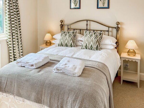 Un lit bien fait, recouvert d’une couvre-lit à motifs, avec deux oreillers ornés de motifs de feuilles, deux lampes de chevet et une fenêtre avec des rideaux.