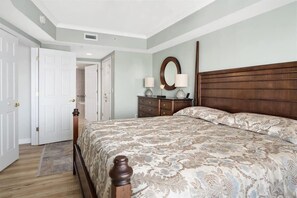 A bedroom with a large bed, a dresser, a mirror, and a door leading to another room. - Large Bayfront Condo with Prime Location and Pool (Ocean City)