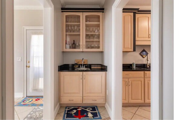 A narrow hallway with a kitchen area featuring wooden cabinets, a black countertop, and a tiled floor.