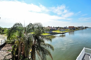 A waterfront property with a dock, palm trees, and a clear view of the water. - Bahia Azul Sunset by Ryson Vacation Rentals (Galveston)