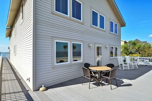 A two-story house with a deck, a dining area with chairs and a table, and a view of the ocean. - Bahia Azul Sunset by Ryson Vacation Rentals (Galveston)