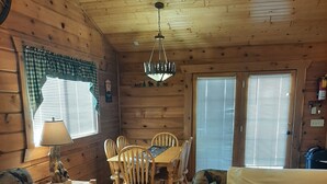 L’intérieur d’un chalet chaleureux, avec une table à manger en bois, des chaises, un canapé et une lampe.