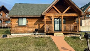 Une cabane en bois dotée d’un porche couvert, d’un barbecue et d’une table de pique-nique.