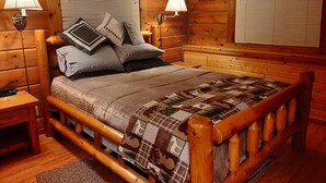 Une chambre à coucher de style cabane en bois, avec un lit, deux lampes de chevet, une table de chevet et une couvre-lit matelassé.