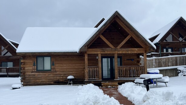 Une cabane en bois, dont le toit et la véranda sont recouverts de neige, et qui est entourée de neige.