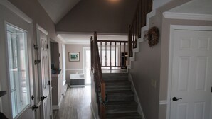 Un couloir avec un escalier menant à un deuxième étage, une porte ornée d’une guirlande et un radiateur fixé au mur.