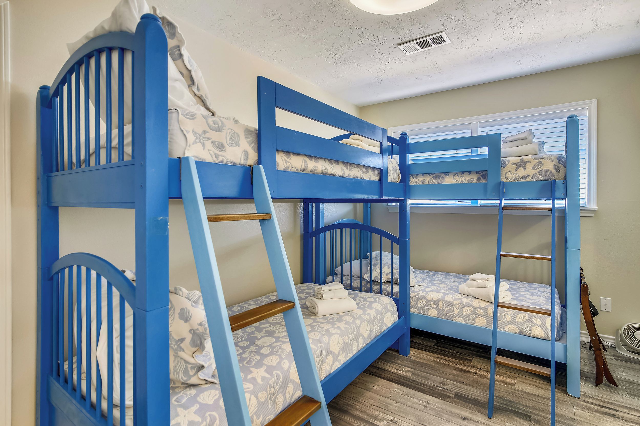 A room with two bunk beds, a wooden ladder, a fan, and a window with blinds.