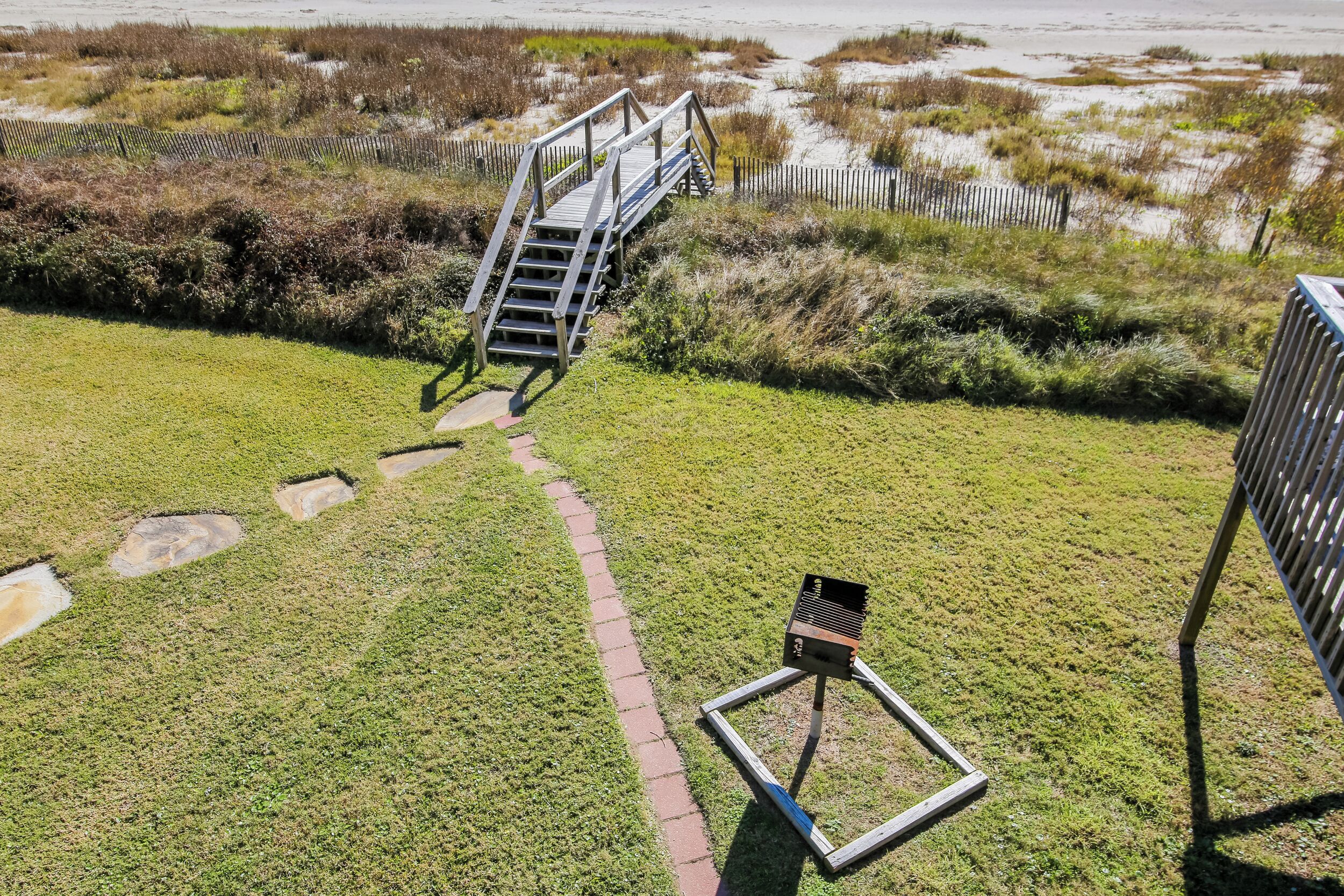A grassy area with a wooden staircase leading to a higher platform, a metal structure, and a paved path.