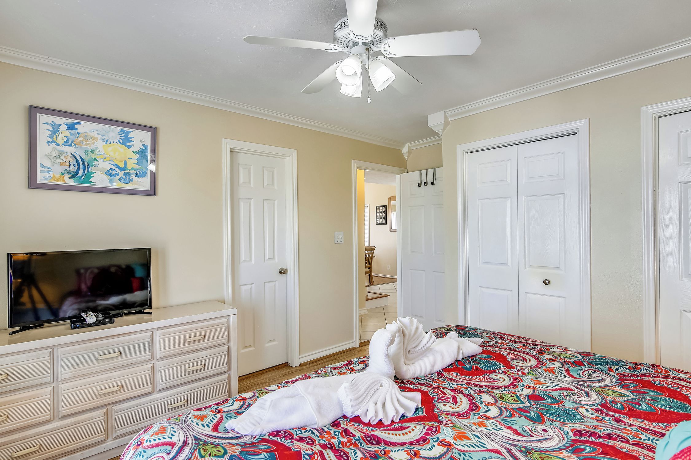 A hotel room with a bed, a TV on a dresser, and a ceiling fan.