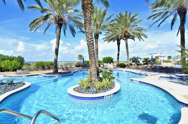 Relax by the serene pool surrounded by lush palm trees and tropical plants, with lounge chairs and umbrellas for comfortable seating.