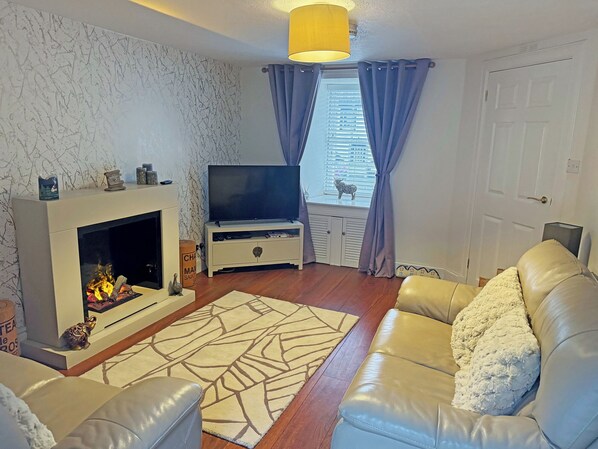A living room with a fireplace, a television, a sofa, and a window with curtains.