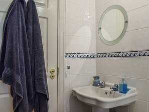 A bathroom with a white sink, a glass mirror, and a towel rack with a dark towel.