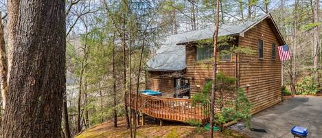 A cabin with a deck, surrounded by trees, and an American flag displayed.