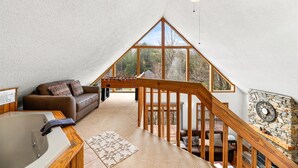 Une chambre mansardée chaleureuse avec un escalier en bois, une grande fenêtre et un ventilateur de plafond.