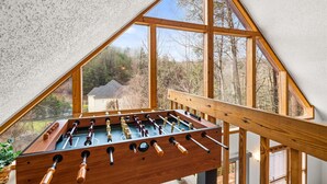 Une table de baby-foot dans une pièce dotée d’un plafond en pente et de grandes fenêtres.