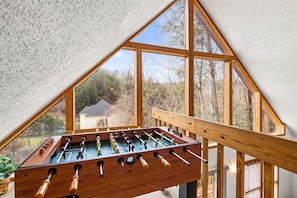 Une table de baby-foot dans une pièce dotée d’un plafond en pente et de grandes fenêtres.