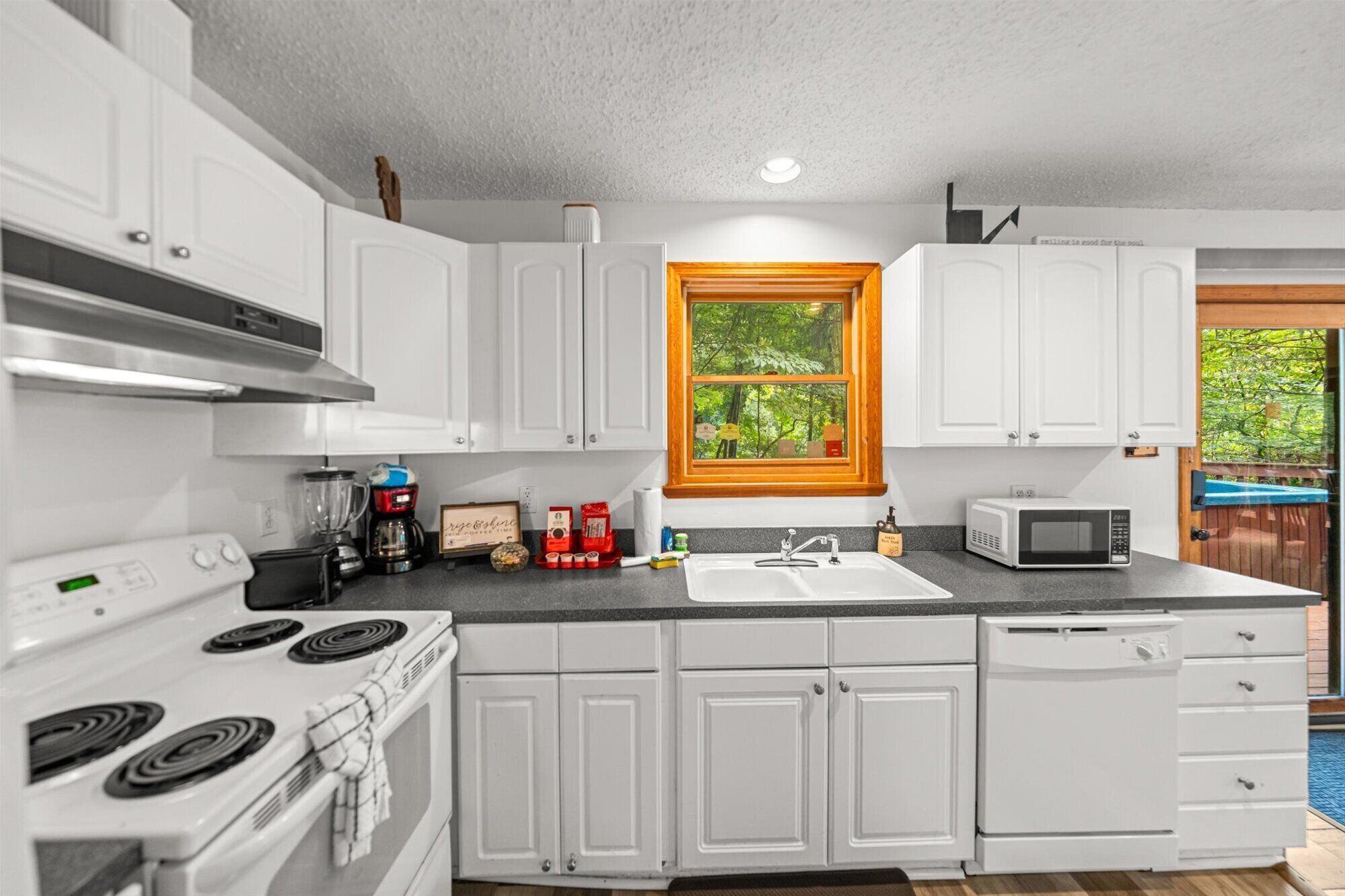 A modern kitchen with white cabinets, a stove, a sink, and a microwave.