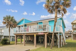 A two-story building with a balcony, palm trees, and a sign indicating vacation rental availability.
