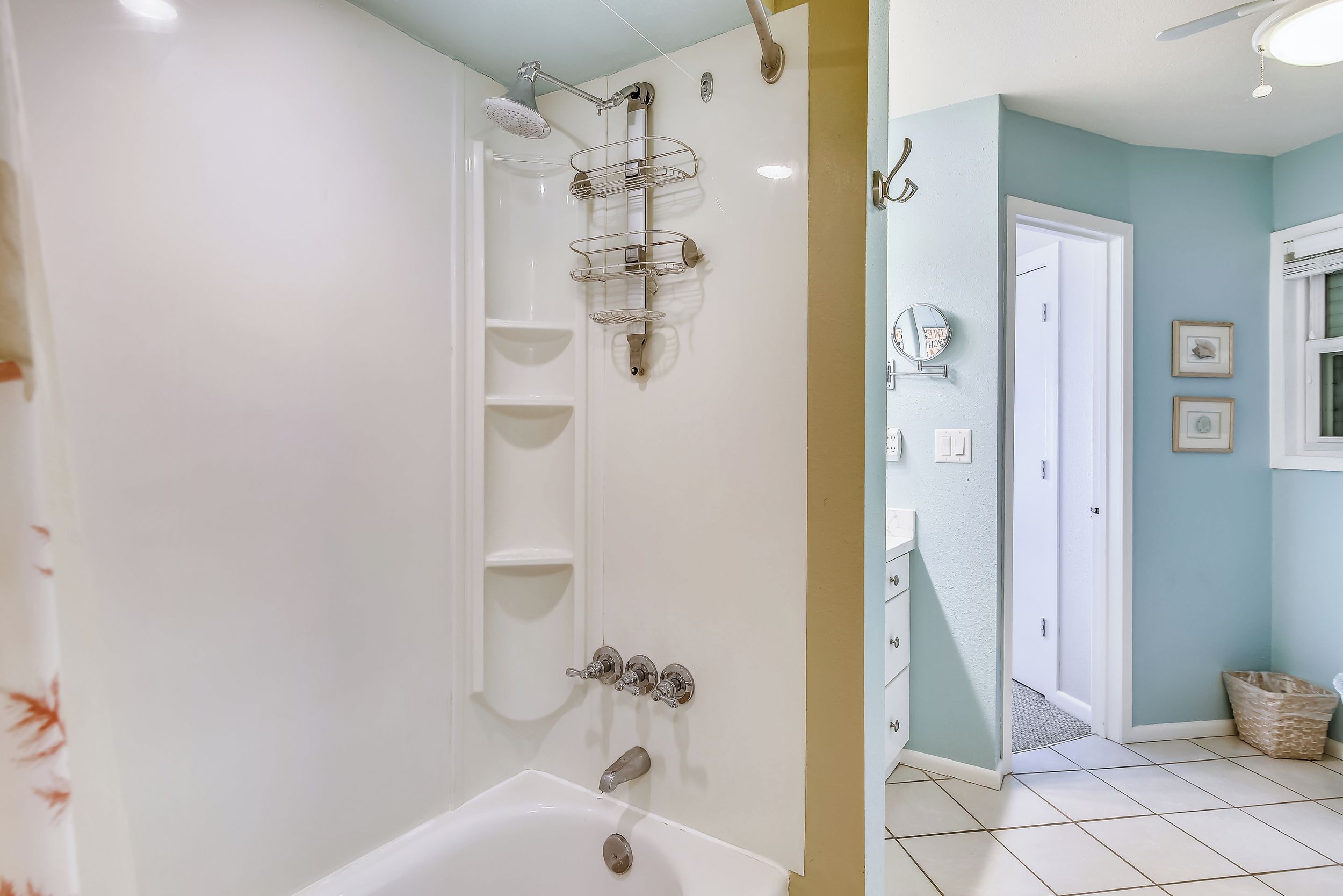 A bathroom with a shower, a bathtub, and a toilet. There are shelves on the wall and a door leading to another room.