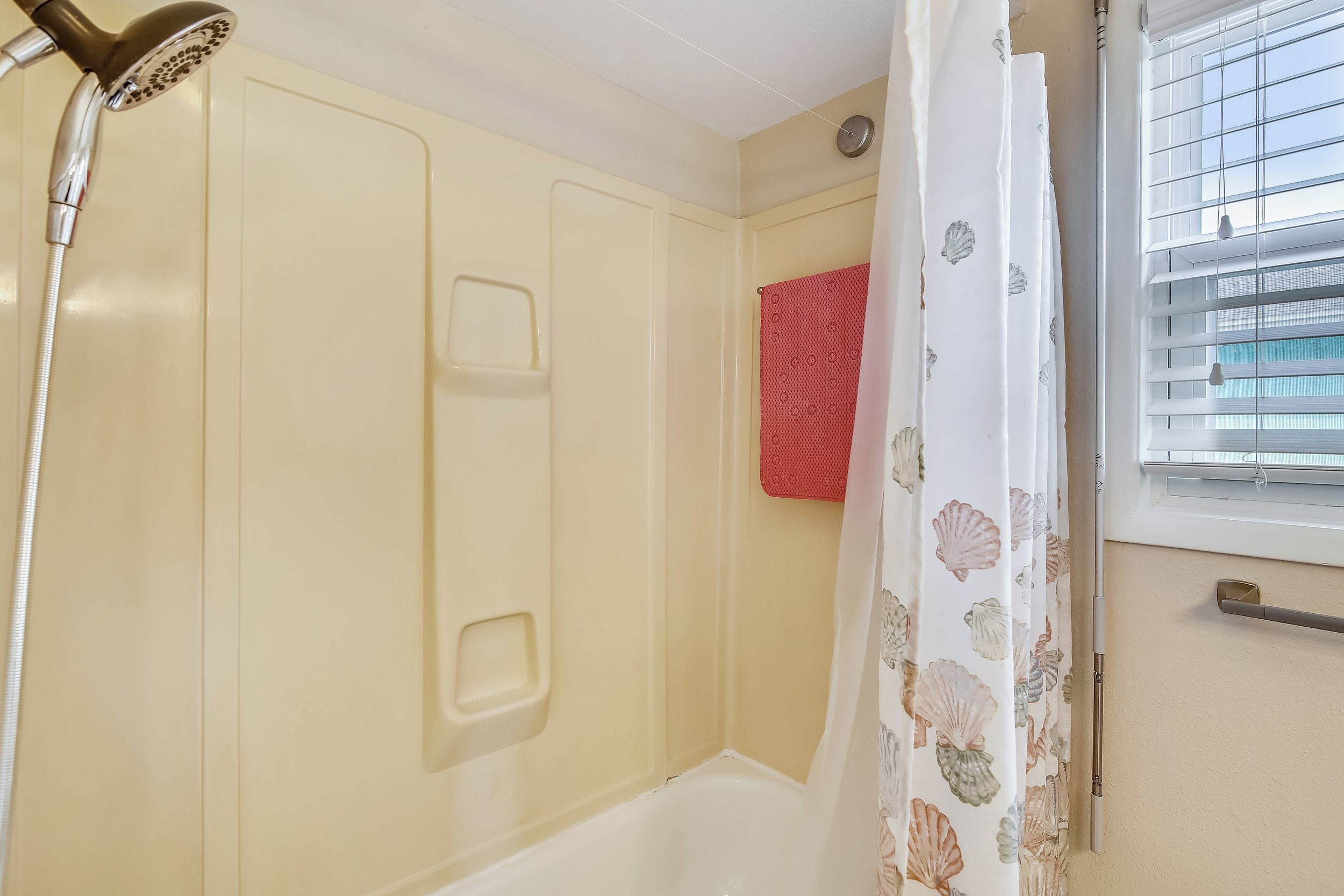 A bathroom with a shower, a bathtub, a window with blinds, and a red towel rack.